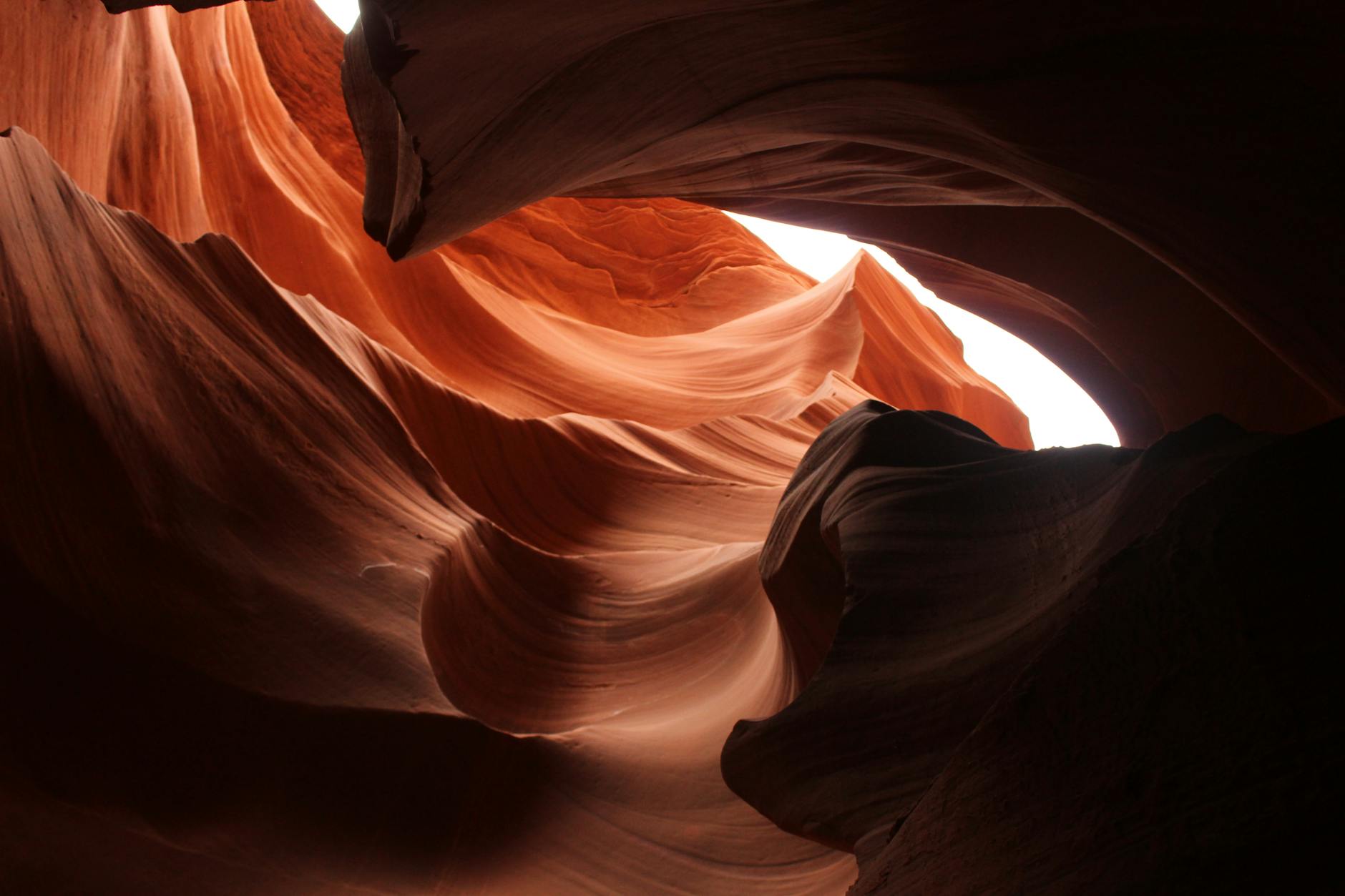 The rocky sides of a cayon undulate. The canyon in the foreground is dark while the light illuminated the rock in the background making like an abstract design.